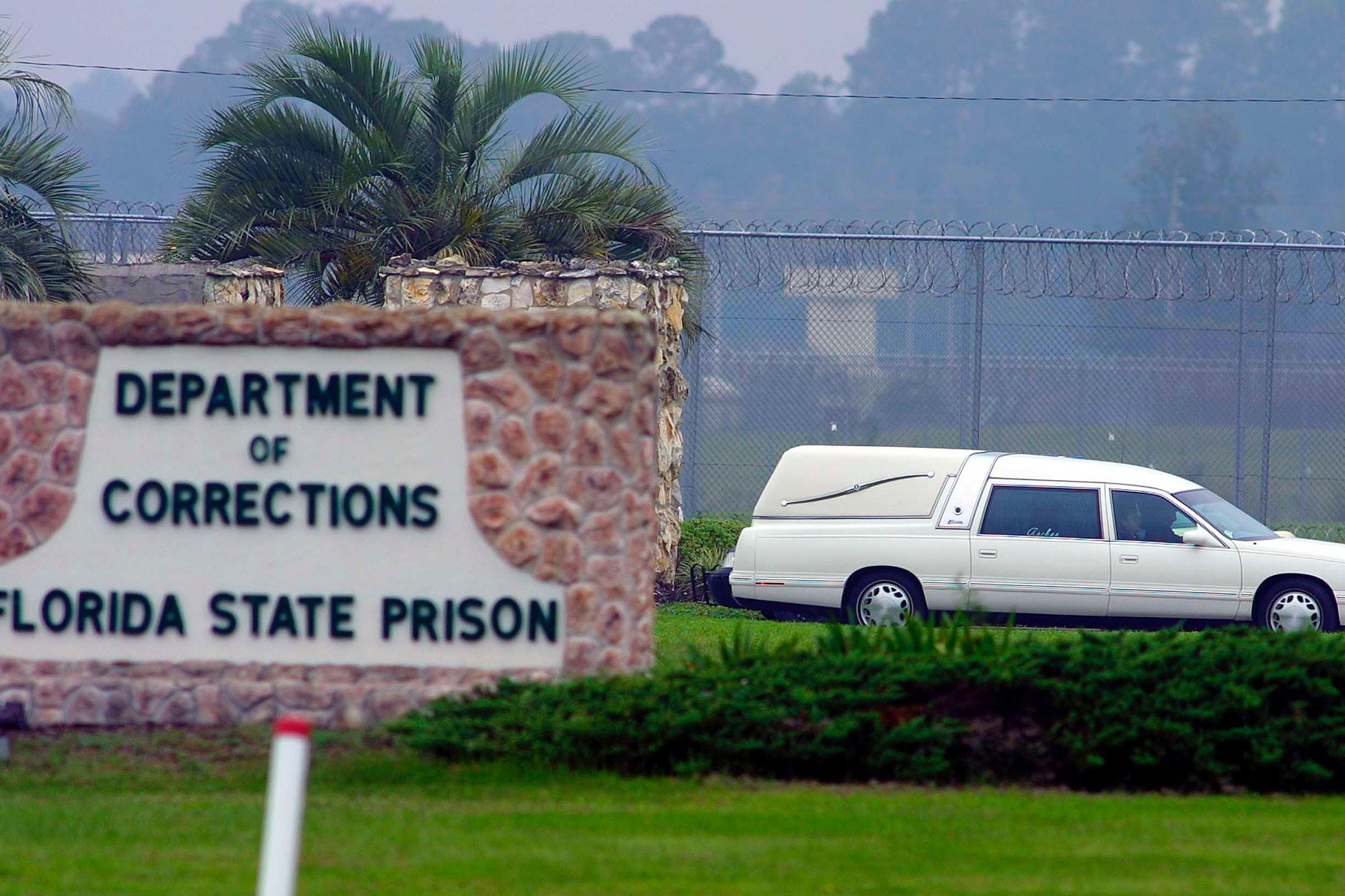 A white hearse drives by a sign for the Florida Department of Corrections