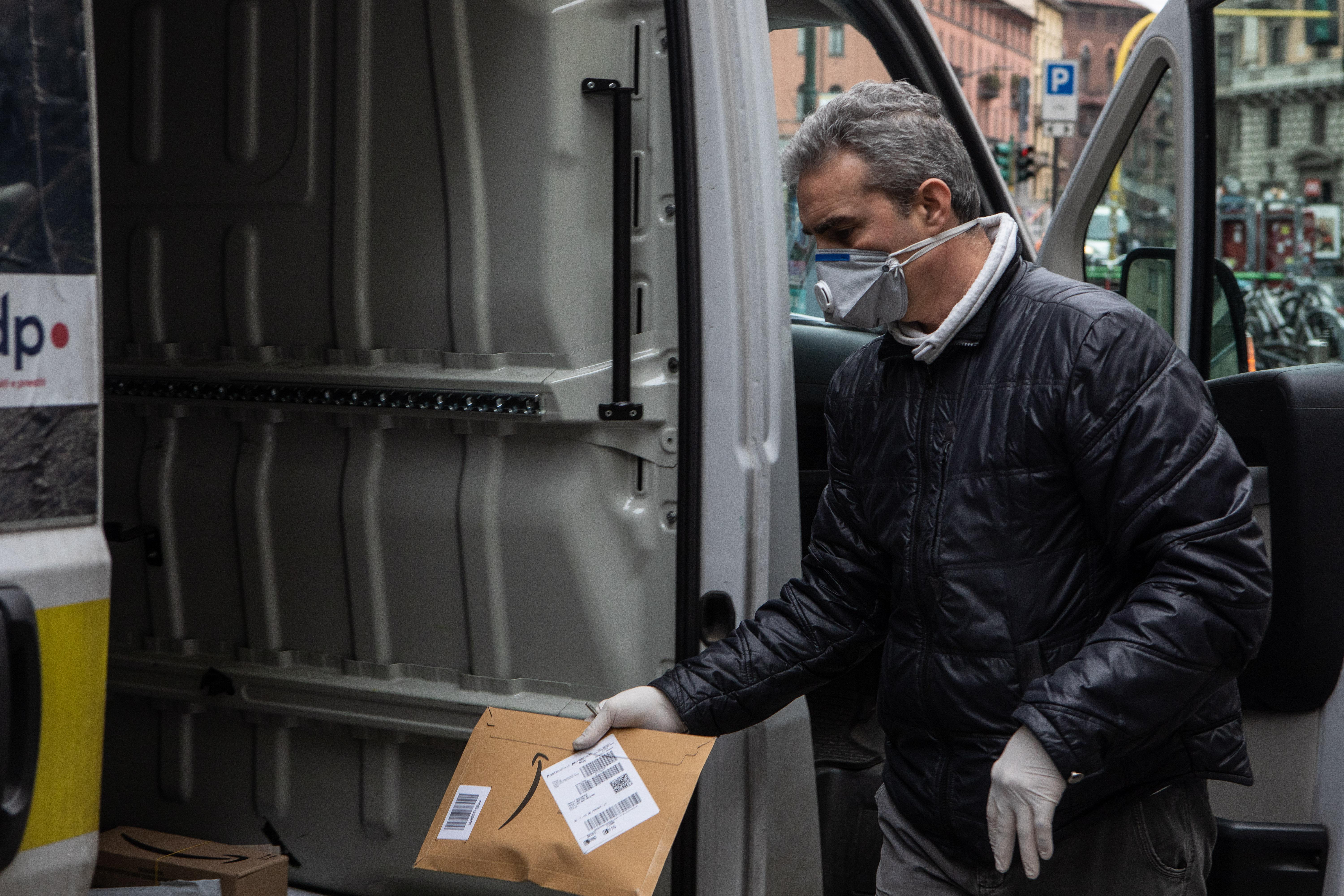 MILAN, ITALY - MARCH 11: A courier, wearing a respiratory mask, handles an Amazon parcel on March 11, 2020 in Milan, Italy. The Italian Government has strengthened up its quarantine rules, shutting all commercial activities except for pharmacies, food shops, gas stations, tobacco stores and news kiosks in a bid to stop the spread of the novel coronavirus. (Photo by Emanuele Cremaschi/Getty Images)