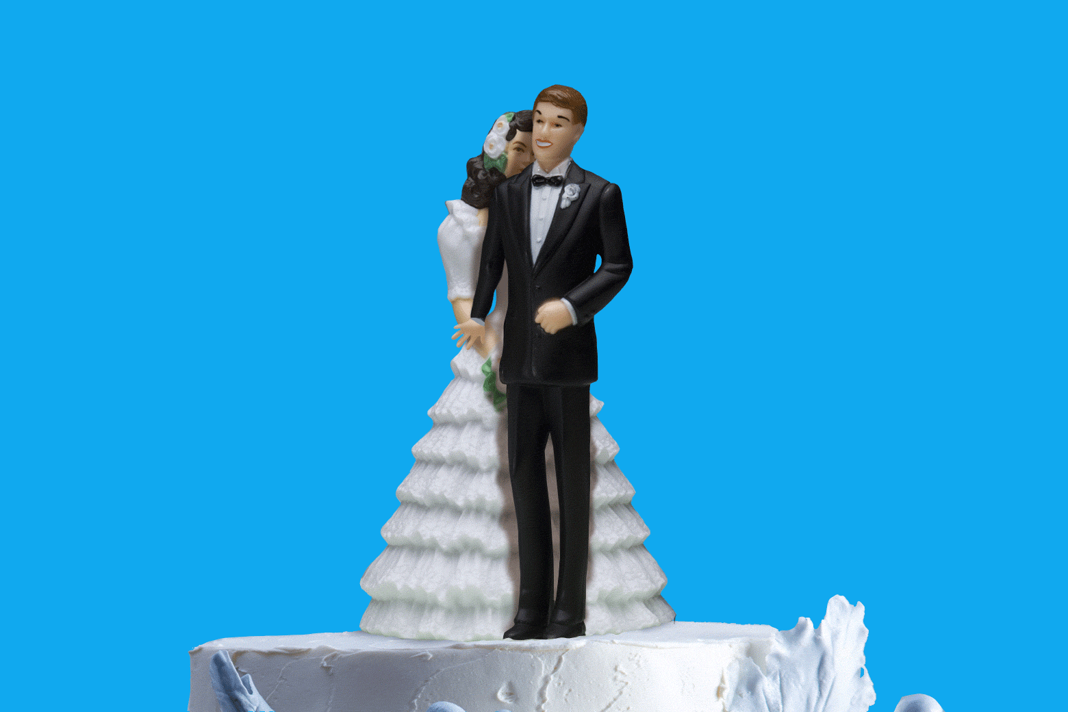 Wedding cake with bride and groom toppers, where the groom is standing in front of the bride.