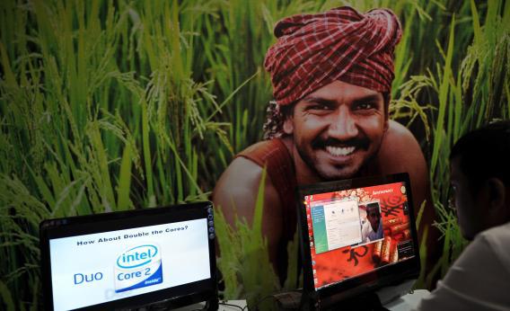 At an IT event in Karnataka, India, an attendee works on a computer in front of a poster of a farmer.