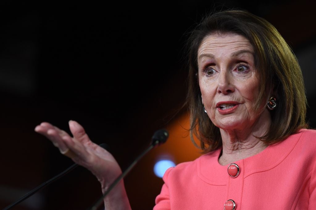 Pelosi gestures with her right hand while speaking into a microphone.