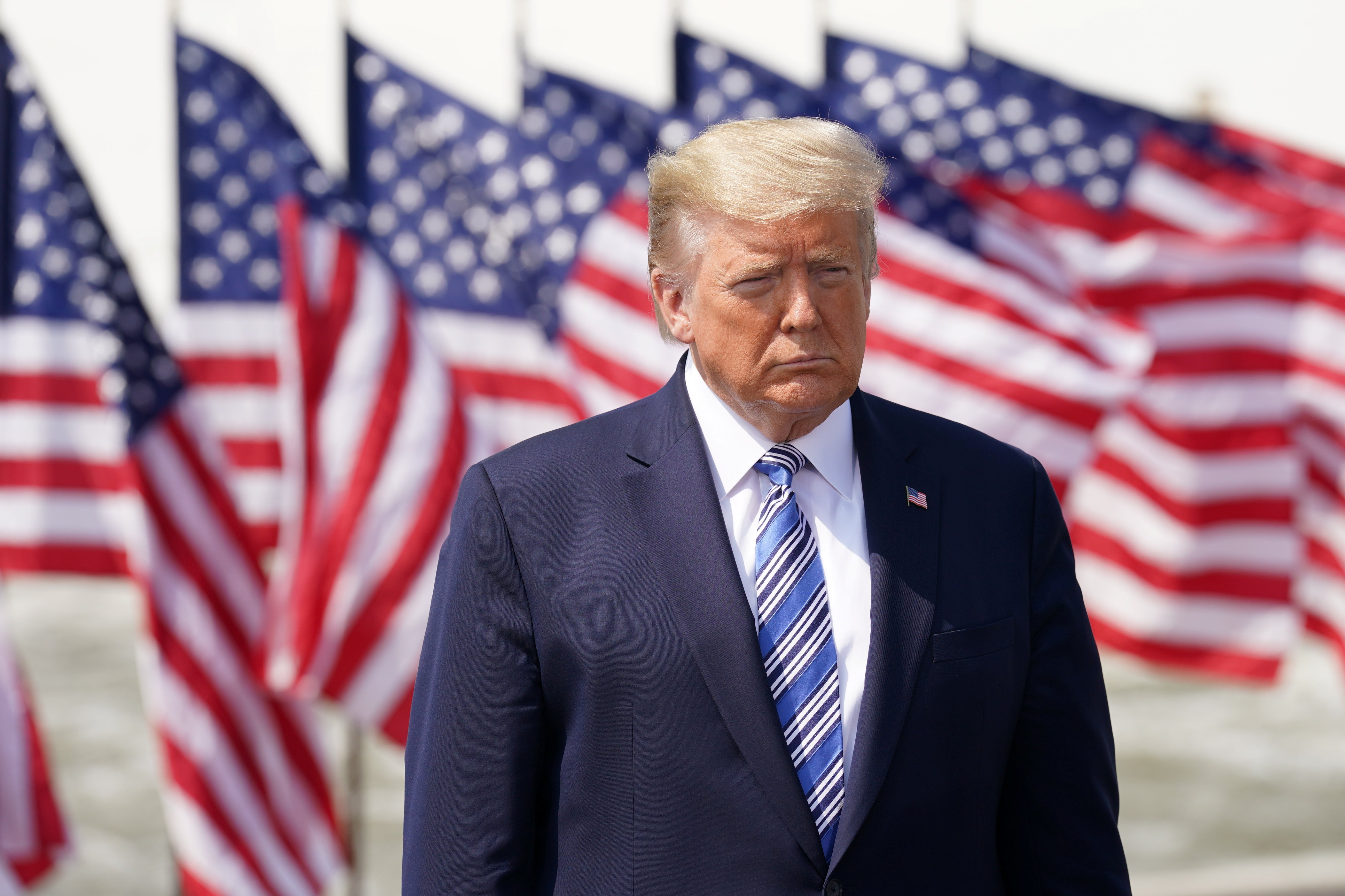 Trump standing in front of a bunch of American flags outside