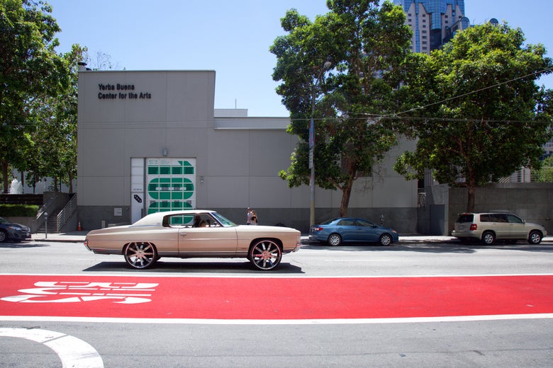 A white car and a red bus lane on a San Francisco street. 