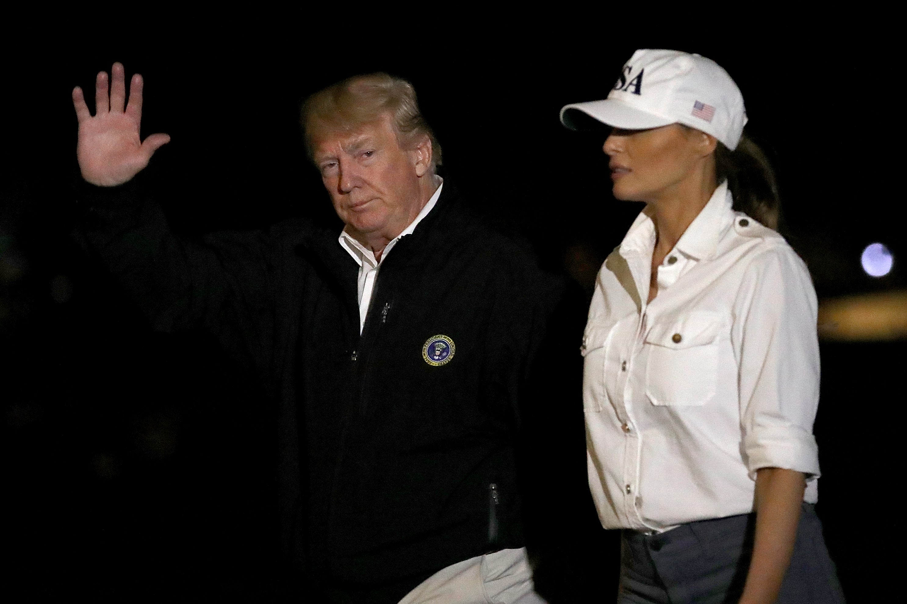Trump, wearing a fleece, waves to the camera while Melania walks alongside him in a baseball cap.