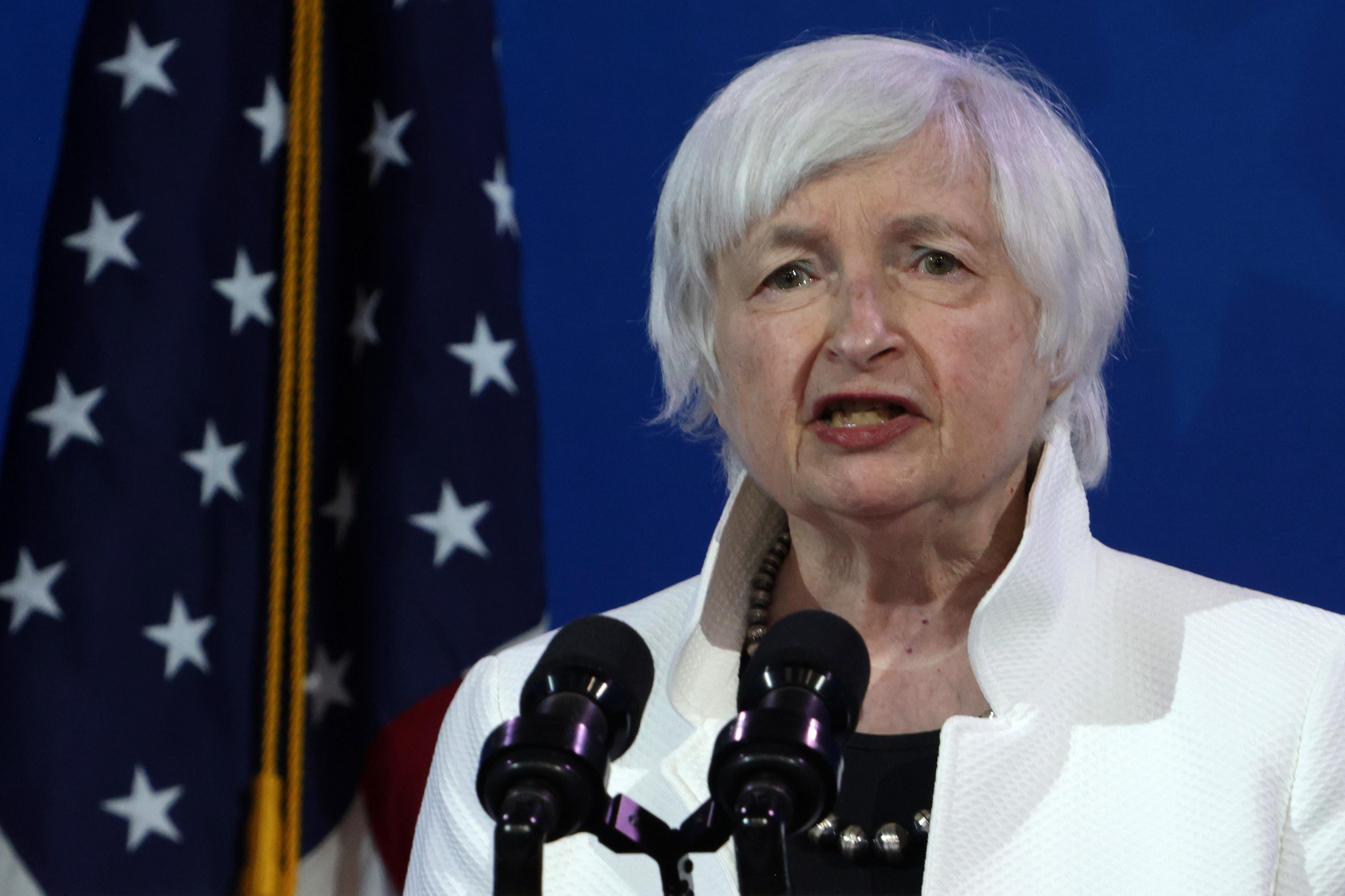 Janet Yellen speaks into a pair of microphones while standing in front of a U.S. flag.