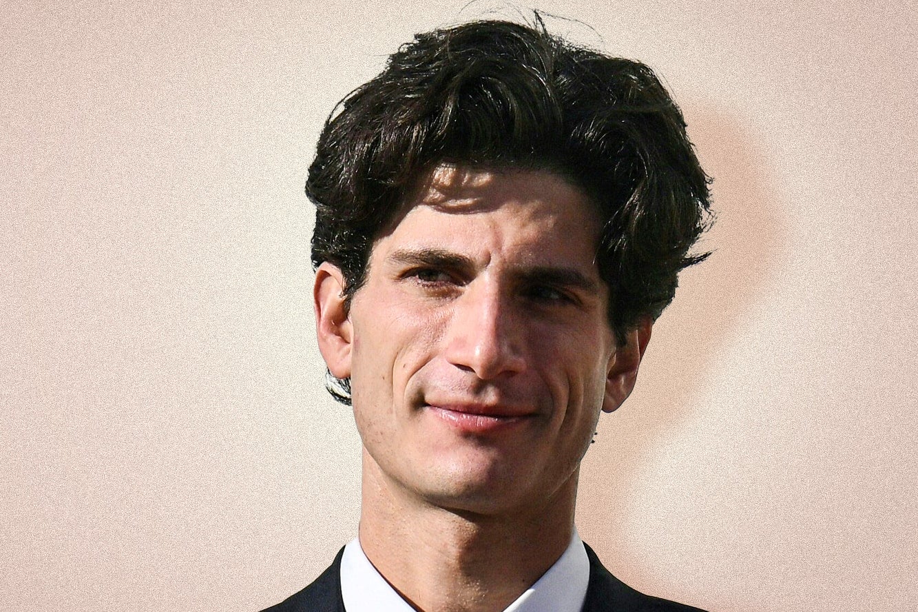 John Schlossberg, a young white man with dark hair, wears a suit and smiles slightly.