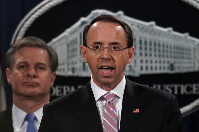 Rosenstein opens his mouth to speak. Behind him are Wray and the DOJ logo.