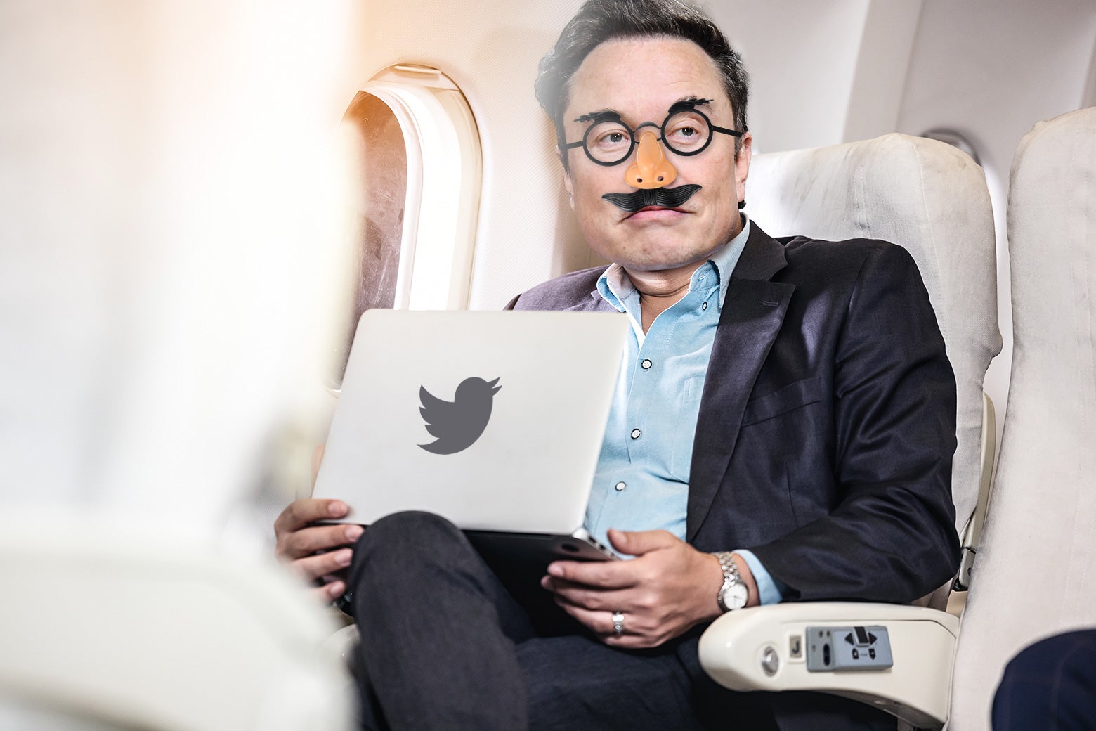 Elon Musk sits in a private plane with a Macbook on his lap and Groucho glasses on his face.