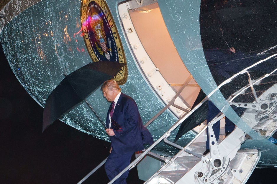 Trump, carrying an umbrella, descends the stairs of a rain-splattered Air Force One.