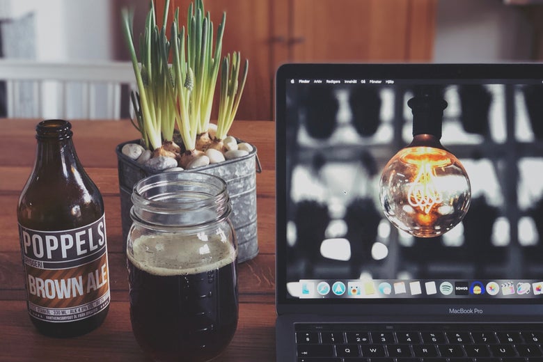 A beer bottle, mason jar, and plant next to a laptop computer