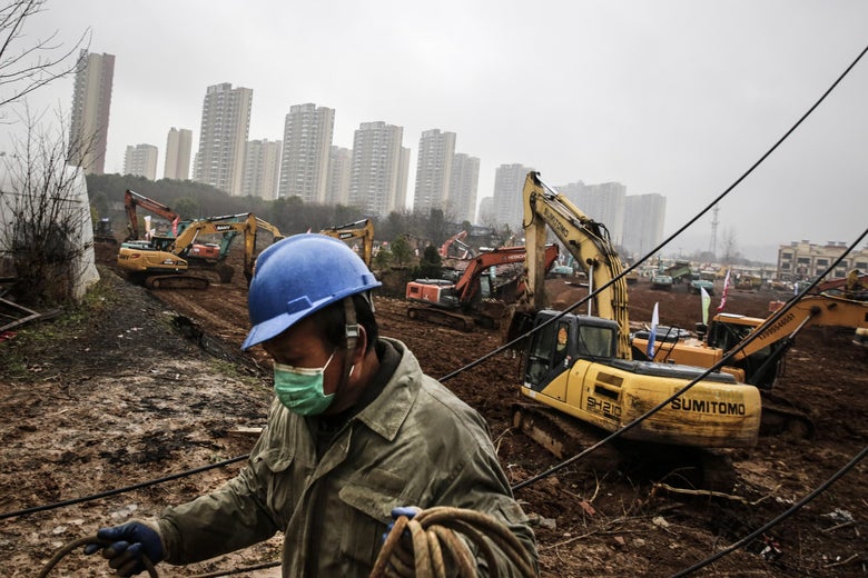 An electrician with a mask works at a busy construction site.