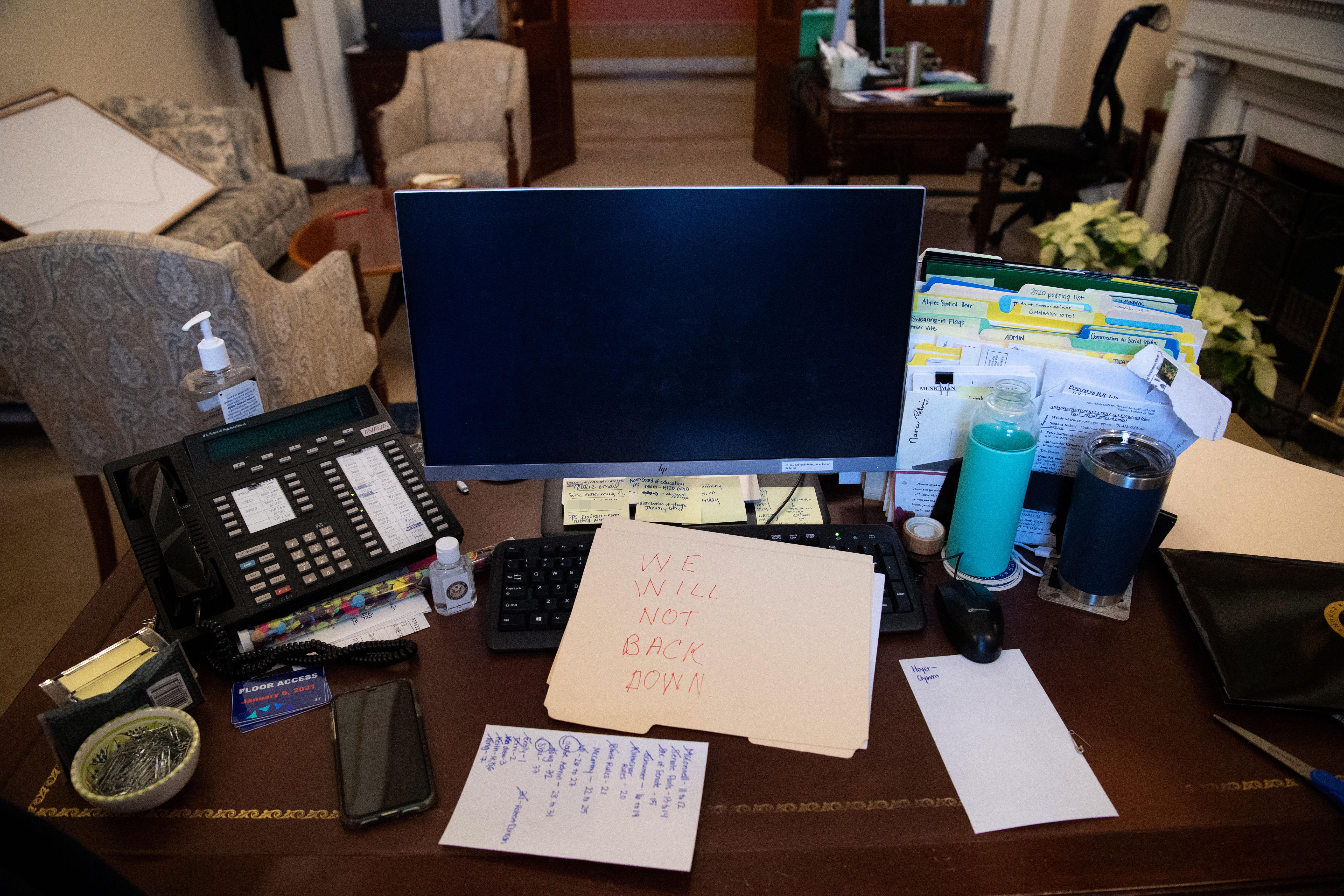 A desk in Pelosi's office with papers, a phone, and a computer on it. A manila folder with "WE WILL NOT BACK DOWN" written on it in red has been placed over the keyboard.