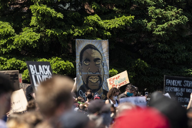 A group of protesters holding signs, including one with an image of George Floyd's face