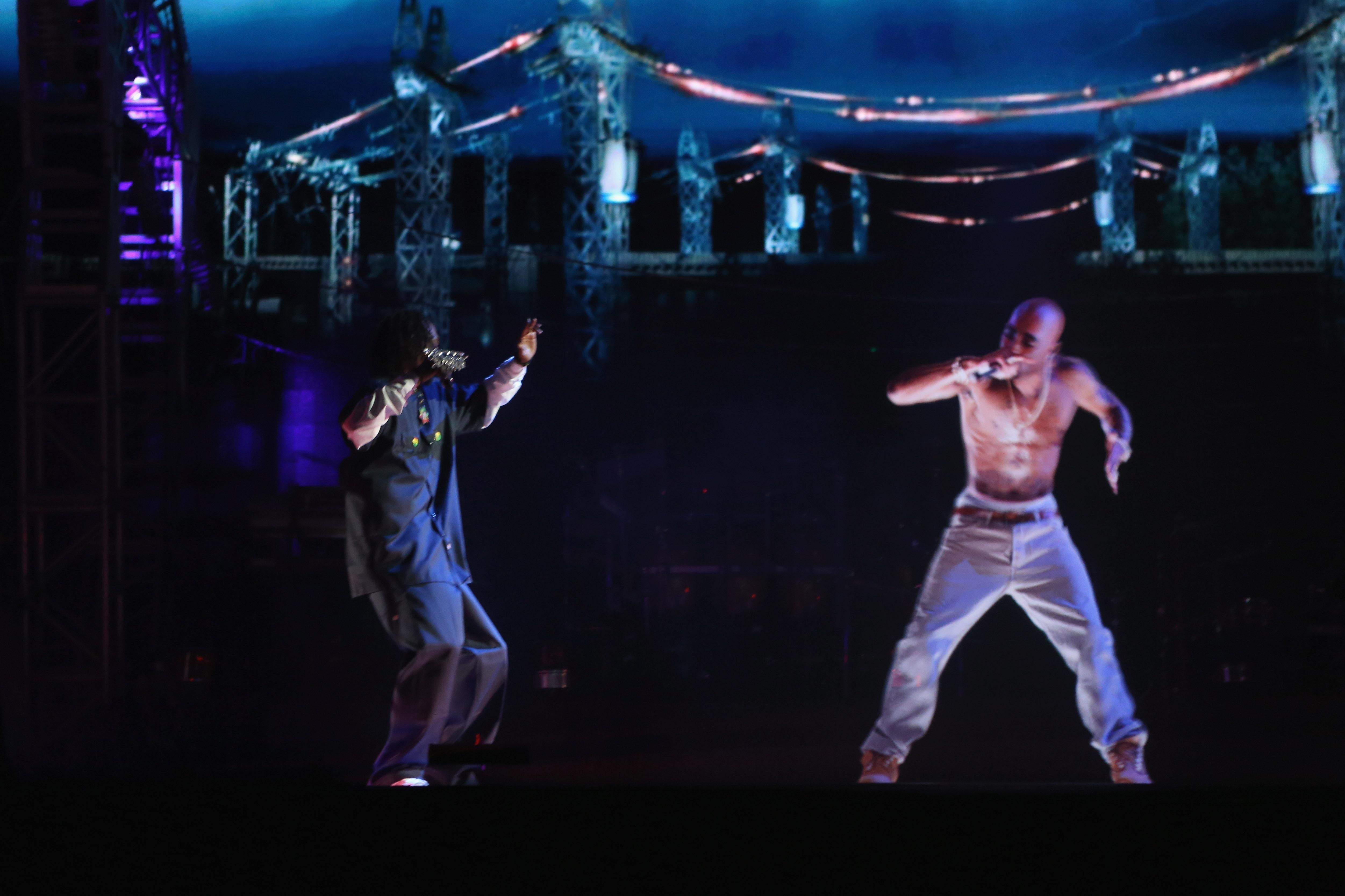 Tupac's hologram rapping into a holographic microphone as Snoop hypes him up on a dark stage