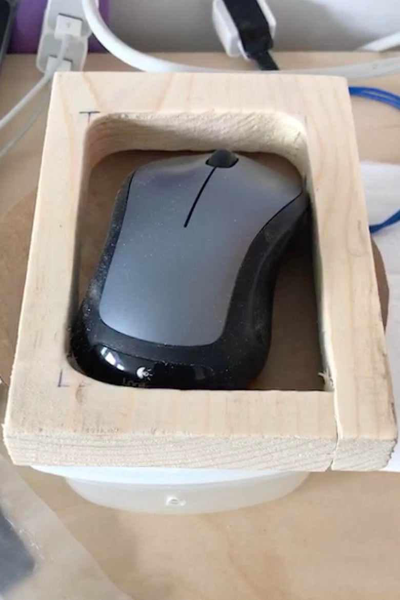 A computer mouse nestled inside a wood frame atop a plastic Tupperware container