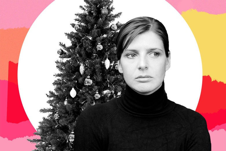A woman in a black turtleneck has a neutral-to-negative expression in front of a Christmas tree.