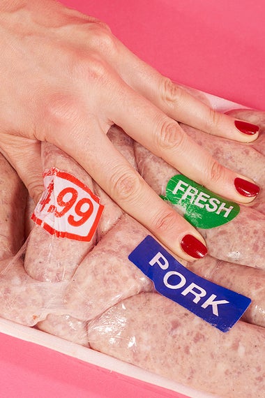A woman's hand pressing down on pork sausage.