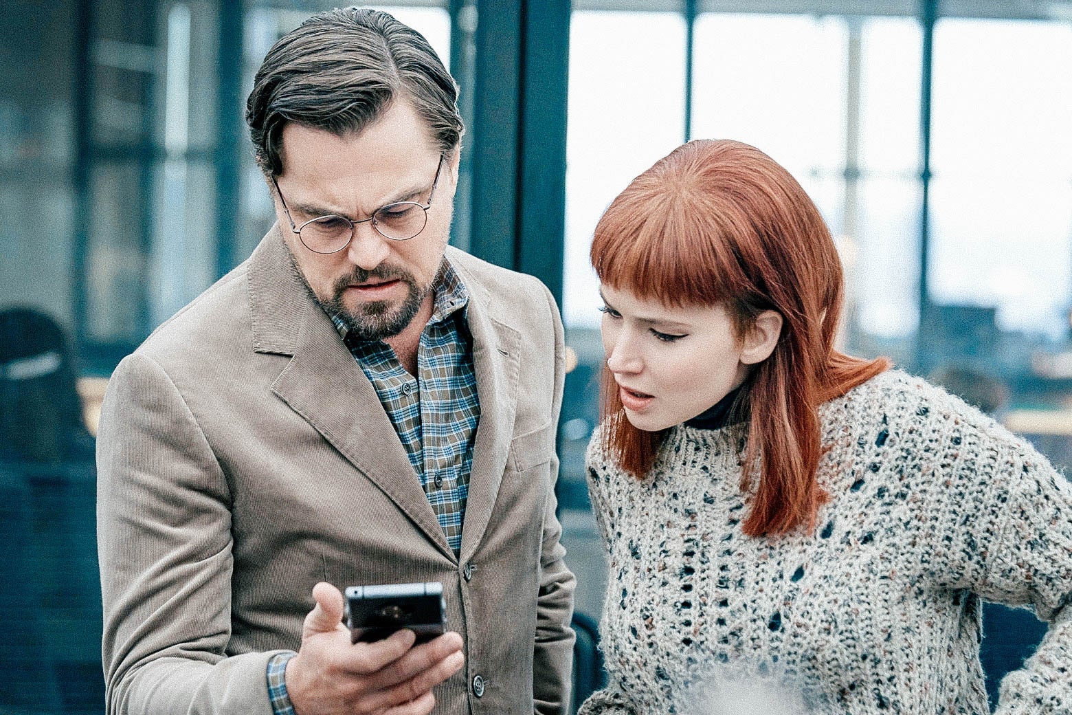 Leonardo DiCaprio and Jennifer Lawrence's characters look down at a smartphone in DiCaprio's hand.