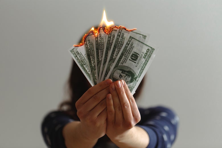 A woman holds several 100 dollar bills, which are on fire. 