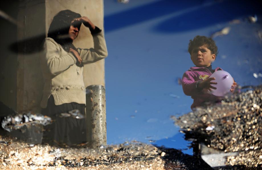 A Syrian internally displaced woman and child are reflected in a puddle of water in the Bab al-Hawa camp along the Turkish border in the northwestern Syrian province of Idlib, on March 18, 2013.