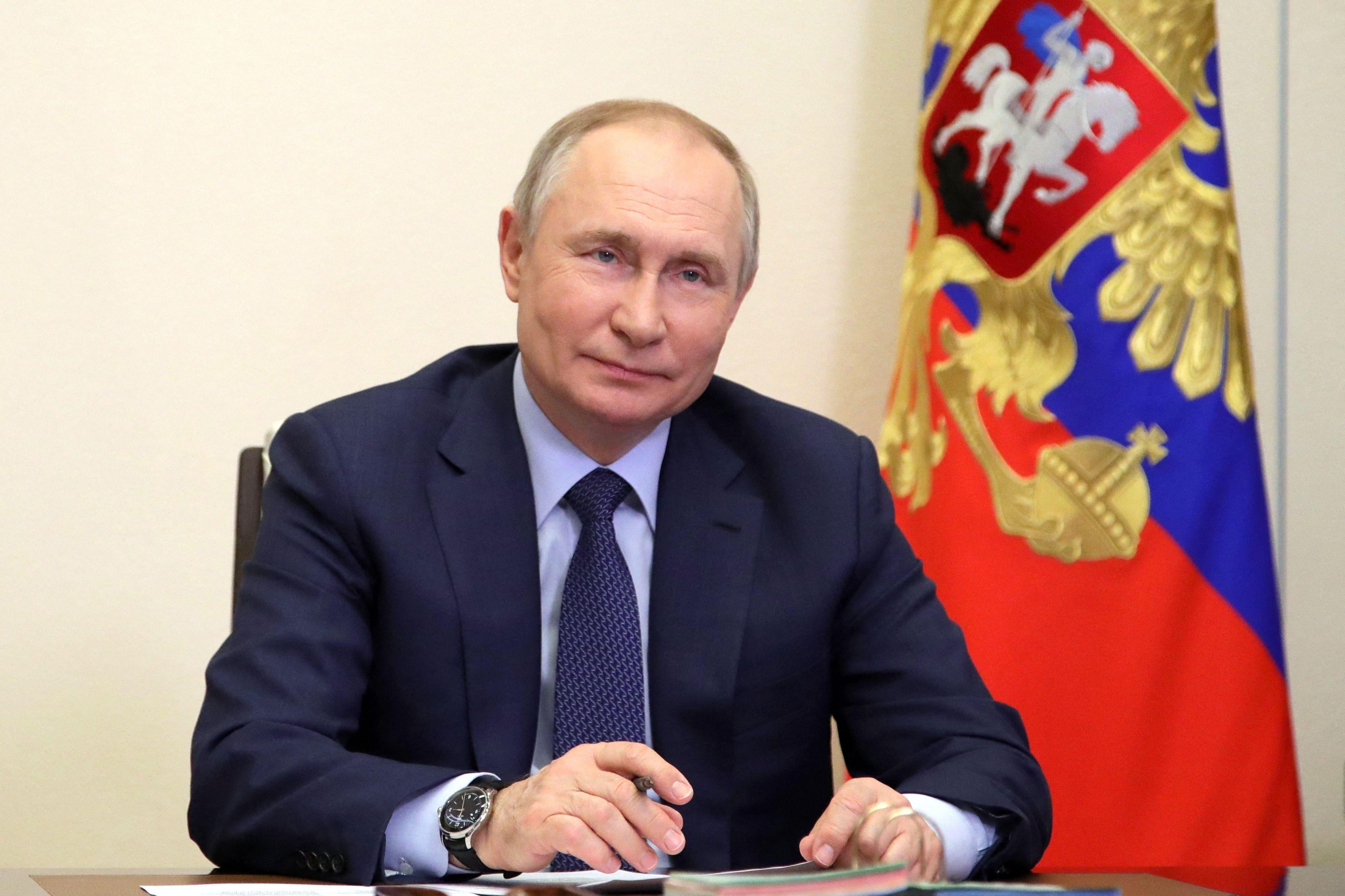 Putin grins next sitting next to the Russian Federation's flag.