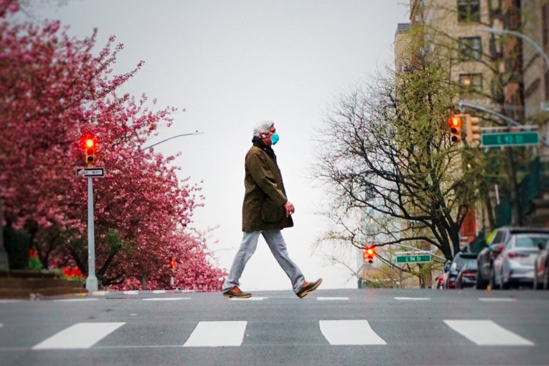 A man walks alone in a crosswalk wearing a mask.