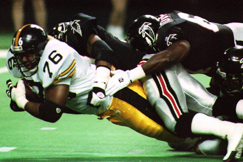 A Pittsburgh player with the ball is tackled by two Atlanta Falcons players.
