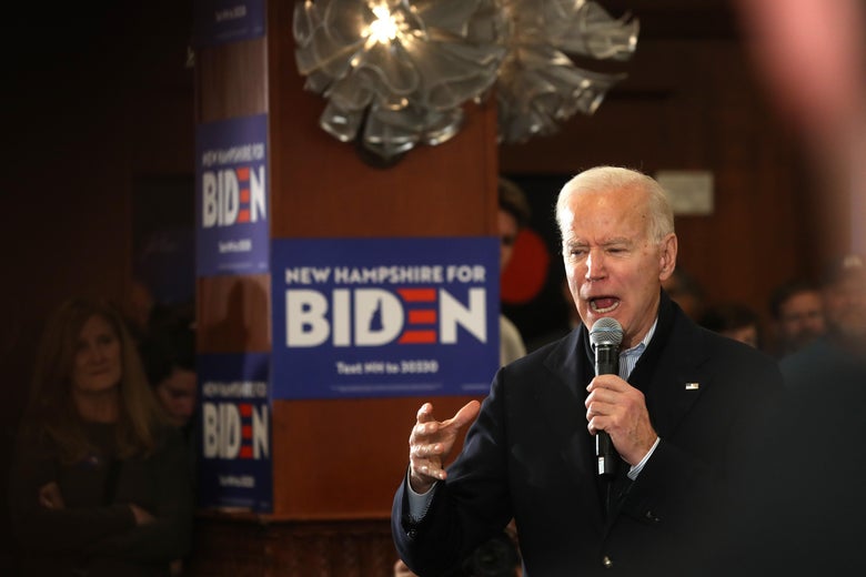 Joe Biden holding a microphone, mid-word, in front of a Biden campaign sign.