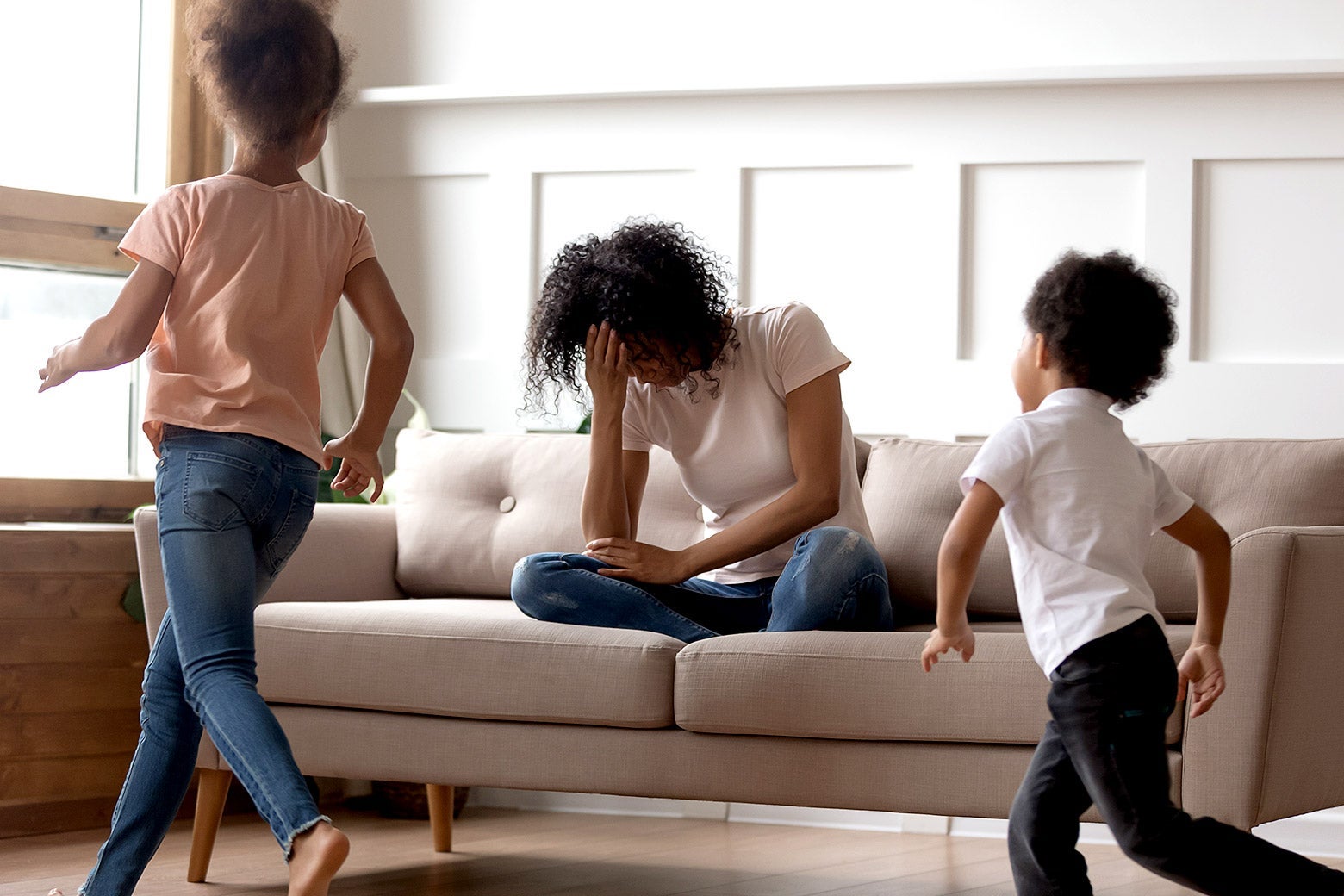 A mom frustrated as her daughter and son run around the living room.