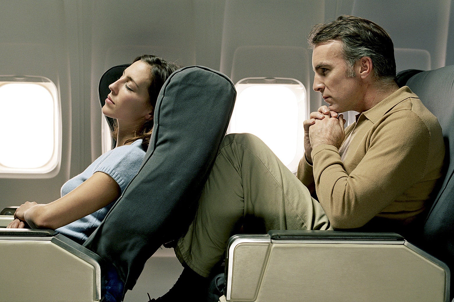 A woman reclining an airplane seat and a man uncomfortable behind her.