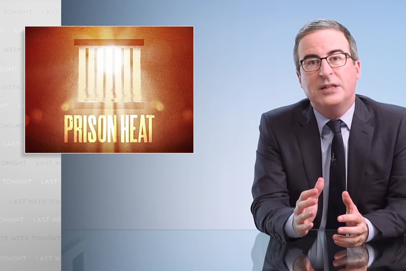 John Oliver sits at a glass anchorperson's desk, in front of an image that is labeled "Prison Heat."