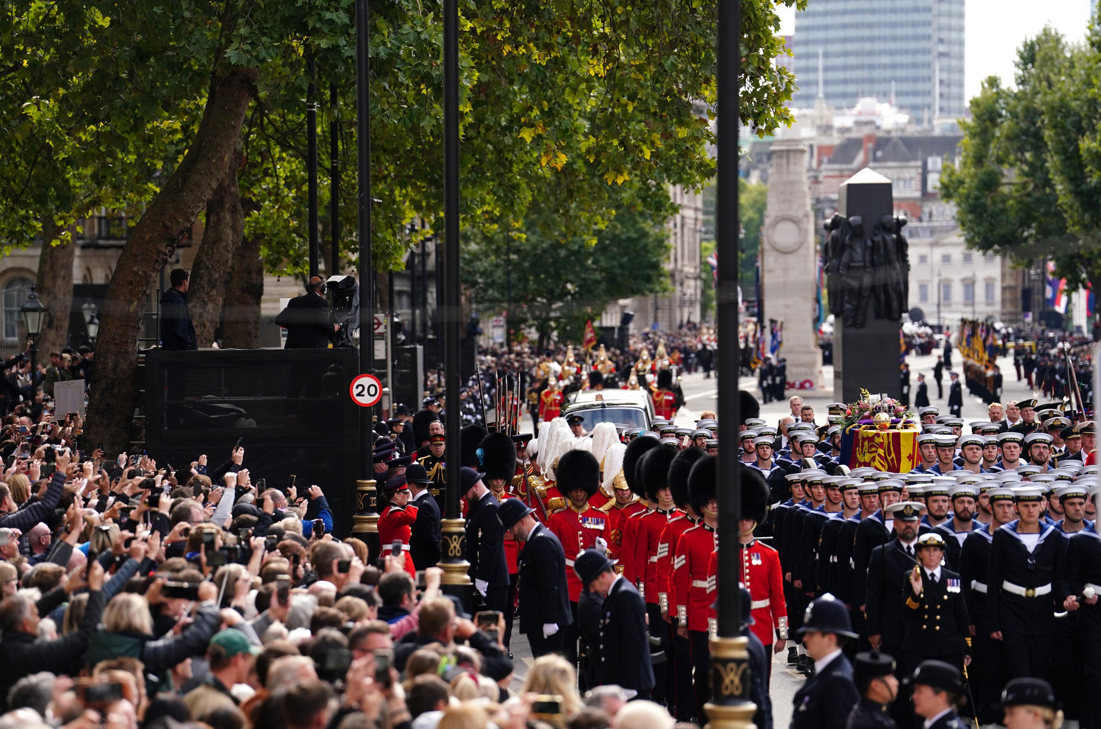 LONDON, ENGLAND - SEPTEMBER 19: Crowds watch as the State Gun Carriage carries the coffin of Queen Elizabeth II, draped in the Royal Standard with the Imperial State Crown and the Sovereign's orb and sceptre, in the Ceremonial Procession following her State Funeral at Westminster Abbey on September 19, 2022 in London, England.  Elizabeth Alexandra Mary Windsor was born in Bruton Street, Mayfair, London on 21 April 1926. She married Prince Philip in 1947 and ascended the throne of the United Kingdom and Commonwealth on 6 February 1952 after the death of her Father, King George VI. Queen Elizabeth II died at Balmoral Castle in Scotland on September 8, 2022, and is succeeded by her eldest son, King Charles III. (Photo by David Davies - WPA Pool/Getty Images)