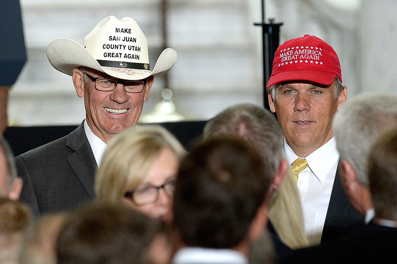 Bruce Adams wears a "Make San Juan County Utah Great Again" cowboy hat and Phil Lyman wears a MAGA hat as they pose for photographs in front of a crowd