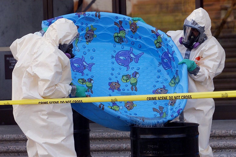 Two people in hazardous materials suits empty a bright blue child's swimming pool into a drum.