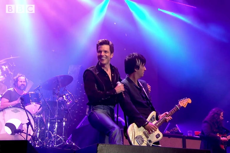 Killers singer Brandon Flowers, on stage at Glastonbury, smiles widely with his arm around Johnny Marr.