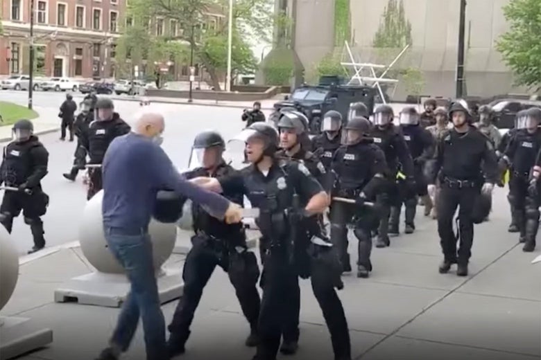 Two cops harass an older man on a sidewalk, as other cops behind them look on.