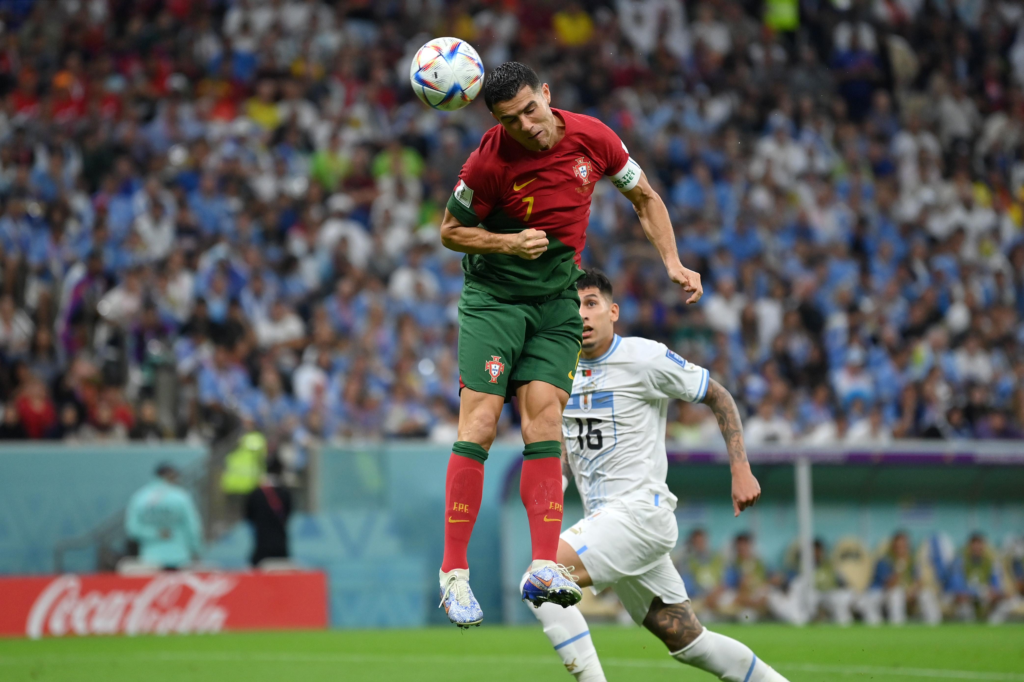 Cristiano Ronaldo of Portugal on the World Cup field as he attempts to head the ball. He has jumped in the air, and the ball almost touches his head. Behind him is one of Uruguay's players.