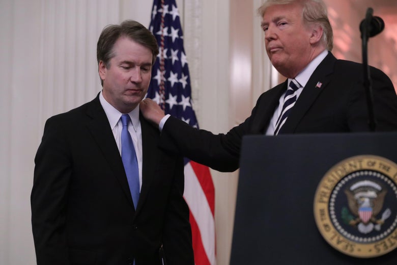 Donald Trump standing at a presidential podium puts his hand on Brett Kavanaugh's shoulder during his swearing-in in 2018