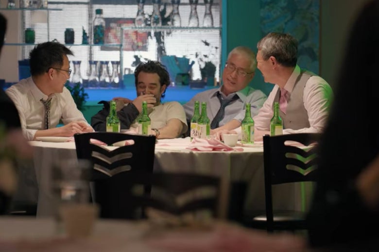 Bill sits with other men at a table at a party.