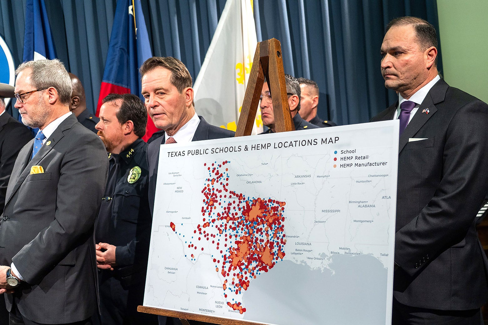At a press conference, a group of politicians stand near a map showing locations of hemp stores and public schools.
