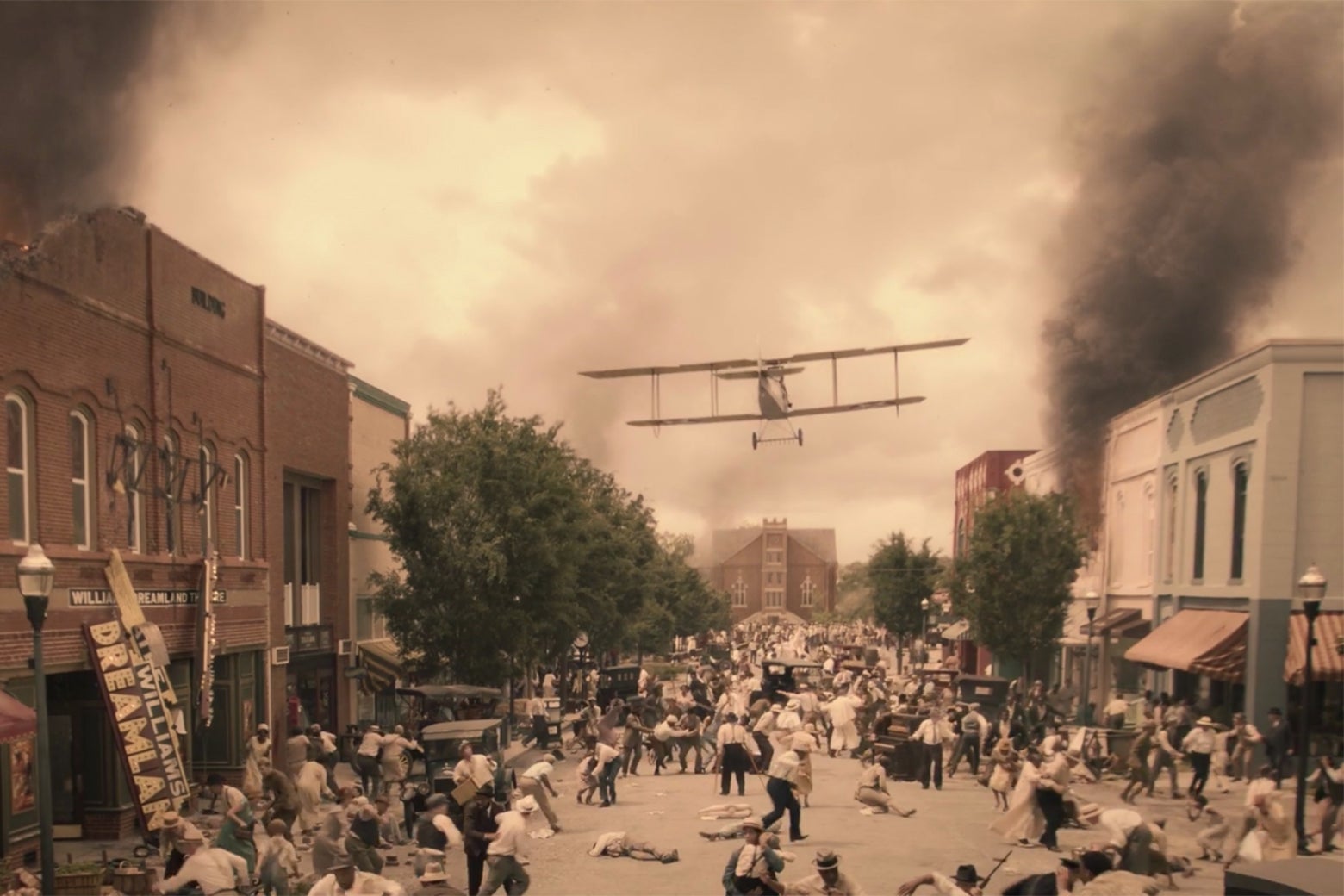 A biplane flies down the main street of Greenwood, above businesses in ruins.
