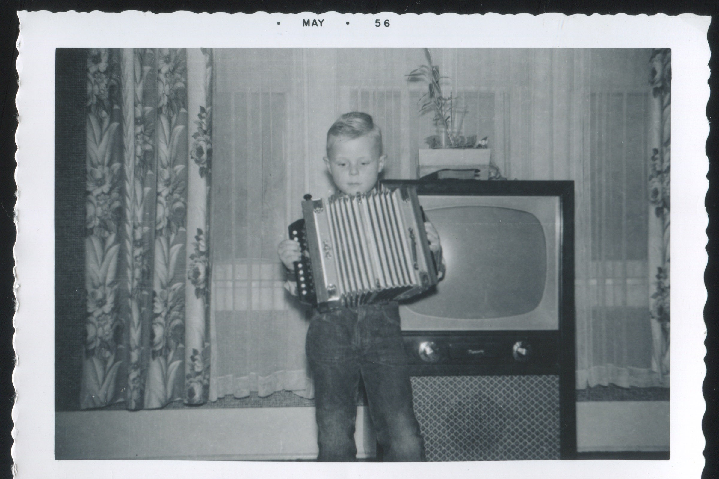 A boy plays an accordion in front of a TV.