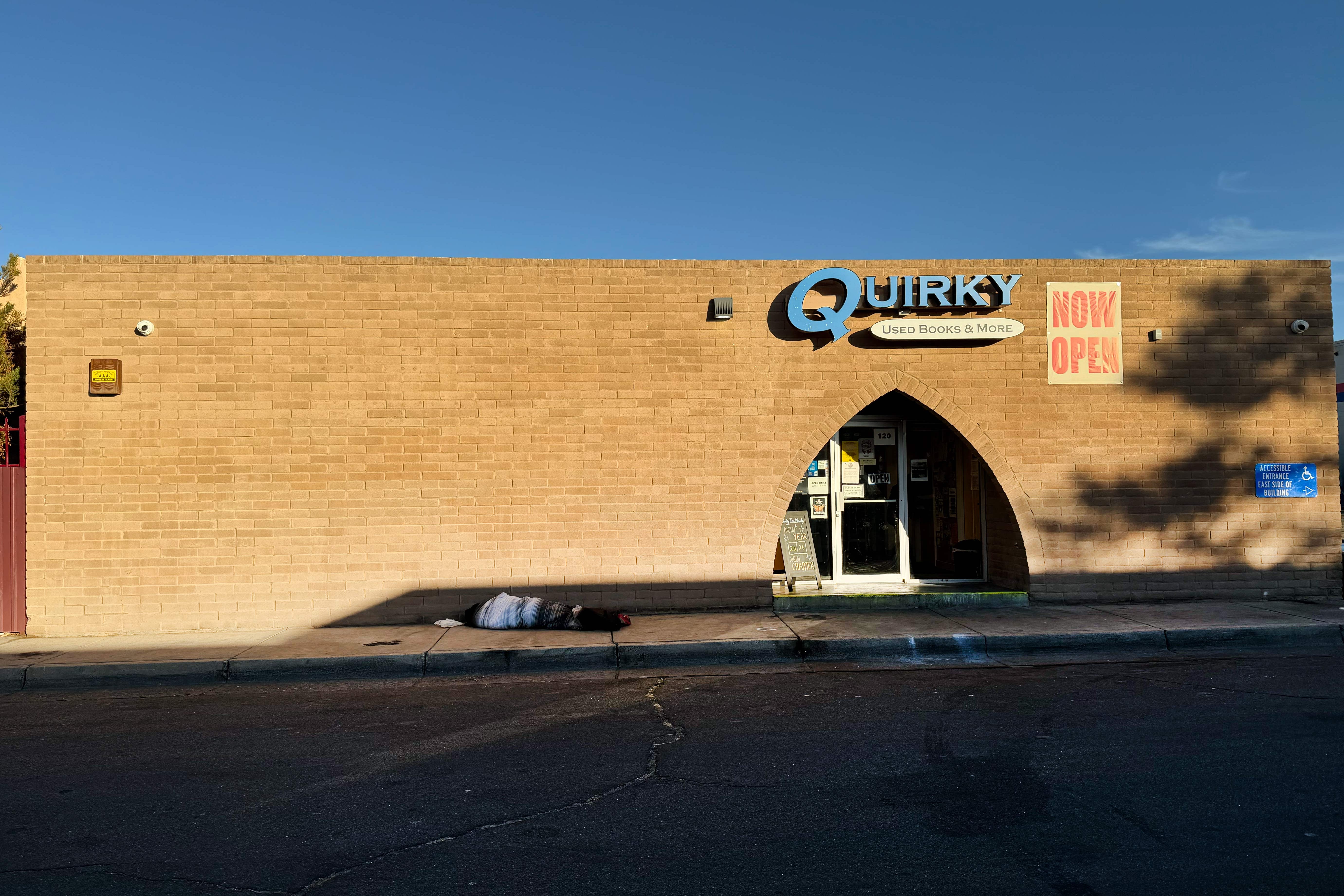 Quirky Bookstore has a "Now Open" sign and a person sleeping on the sidewalk out front. 