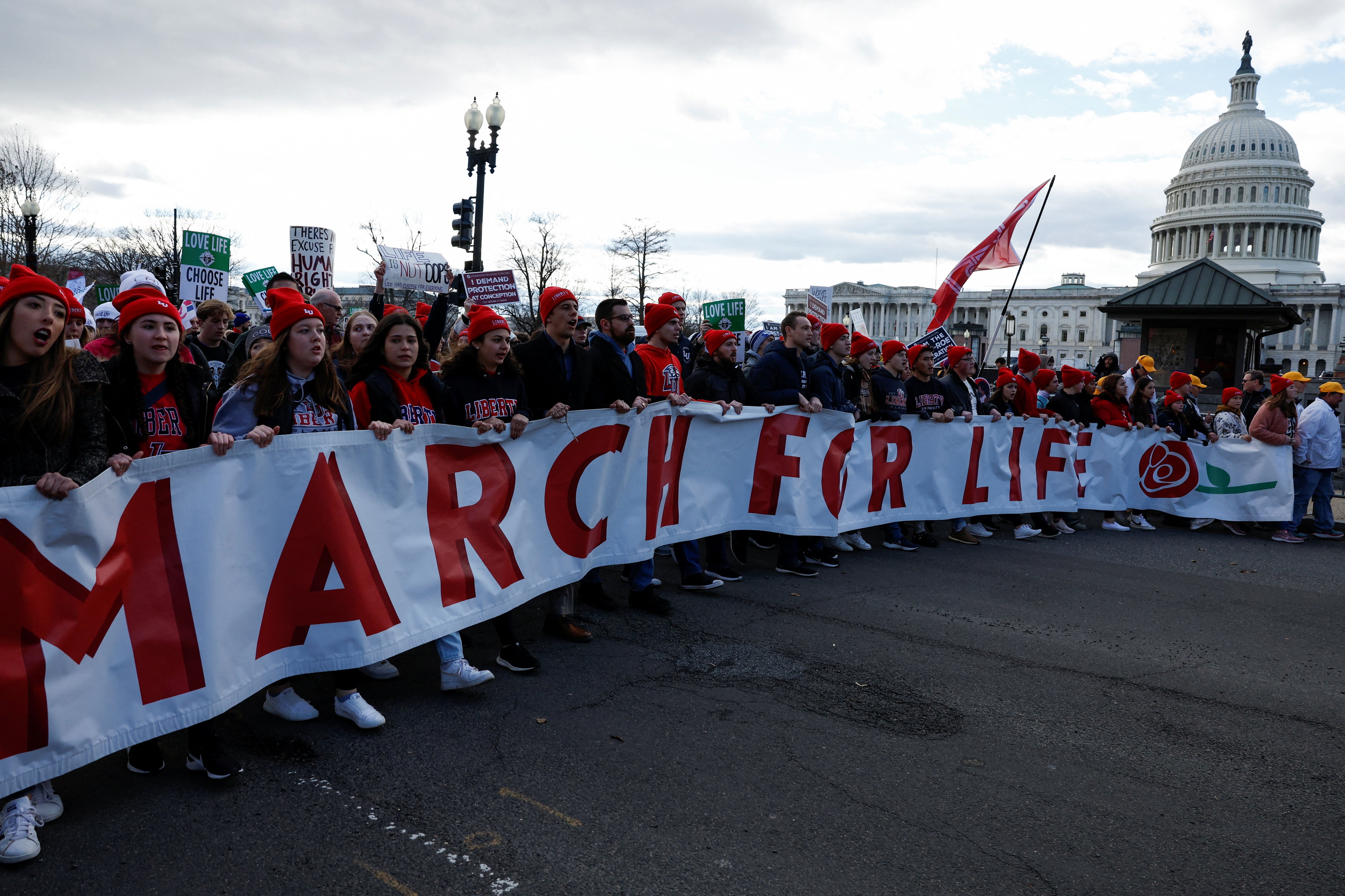 A group of people wearing red hats carry a long sign that says "March for Life."
