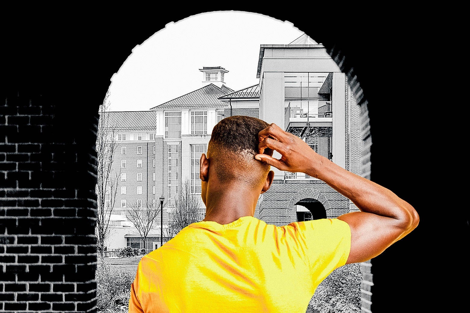 A black man, seen from behind, holds his hand to his head as he looks at campus.