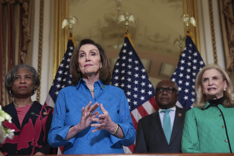 Brenda Lawrence, Nancy Pelosi, Jim Clyburn, and Carolyn Maloney all stand in behind a desk and in front of U.S. flags.