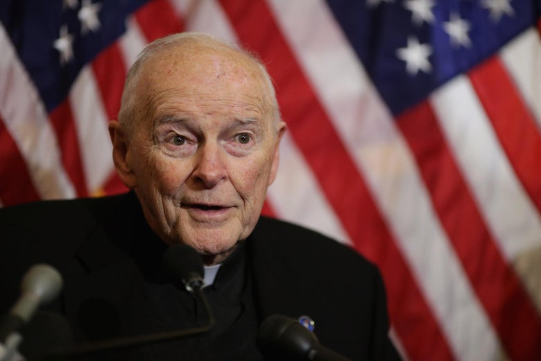 McCarrick speaks into microphones. He sits in front of an American flag backdrop.