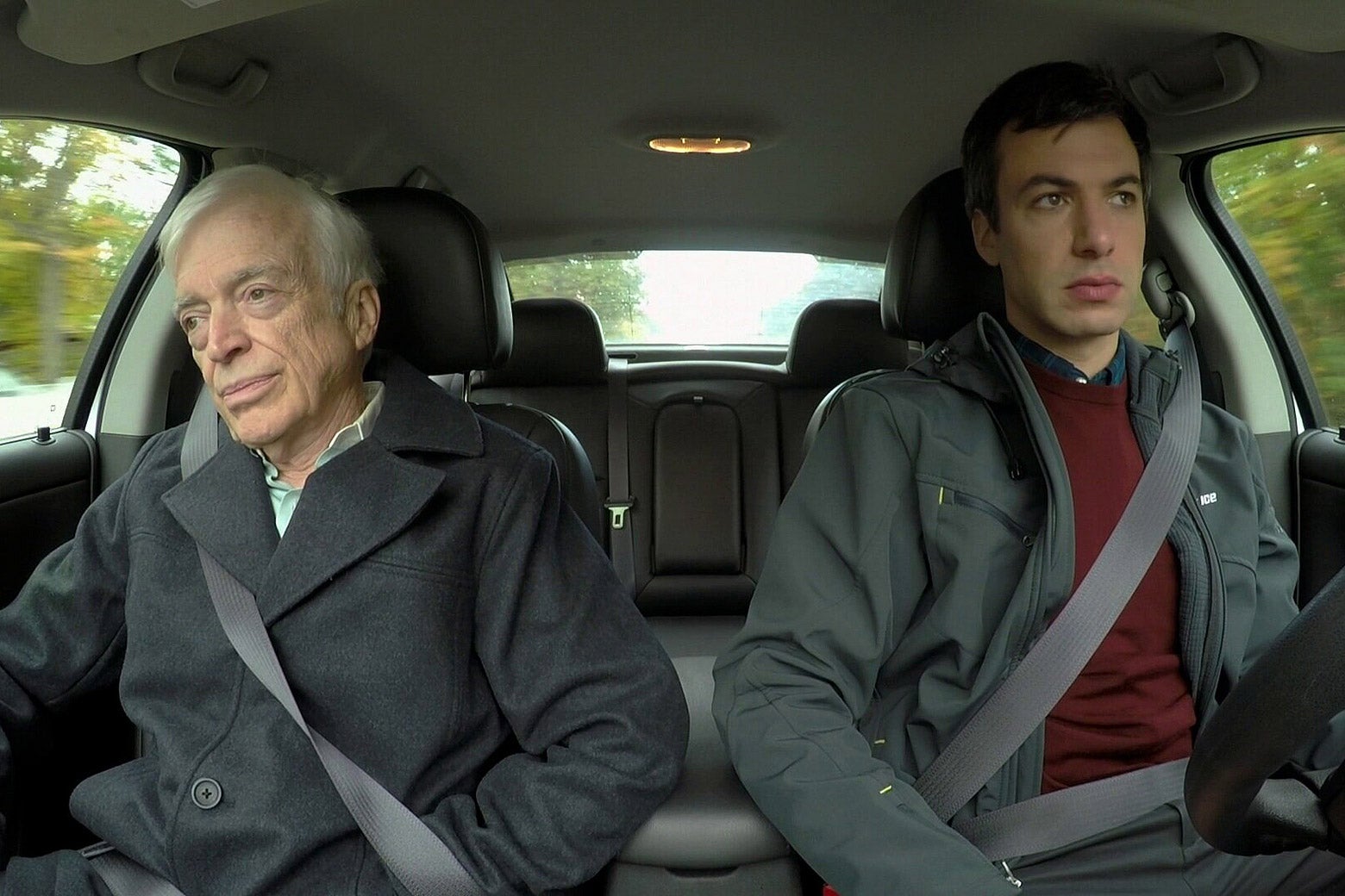 A white-haired white man and a thirtysomething brown-haired white man sit inside a car looking nervous.