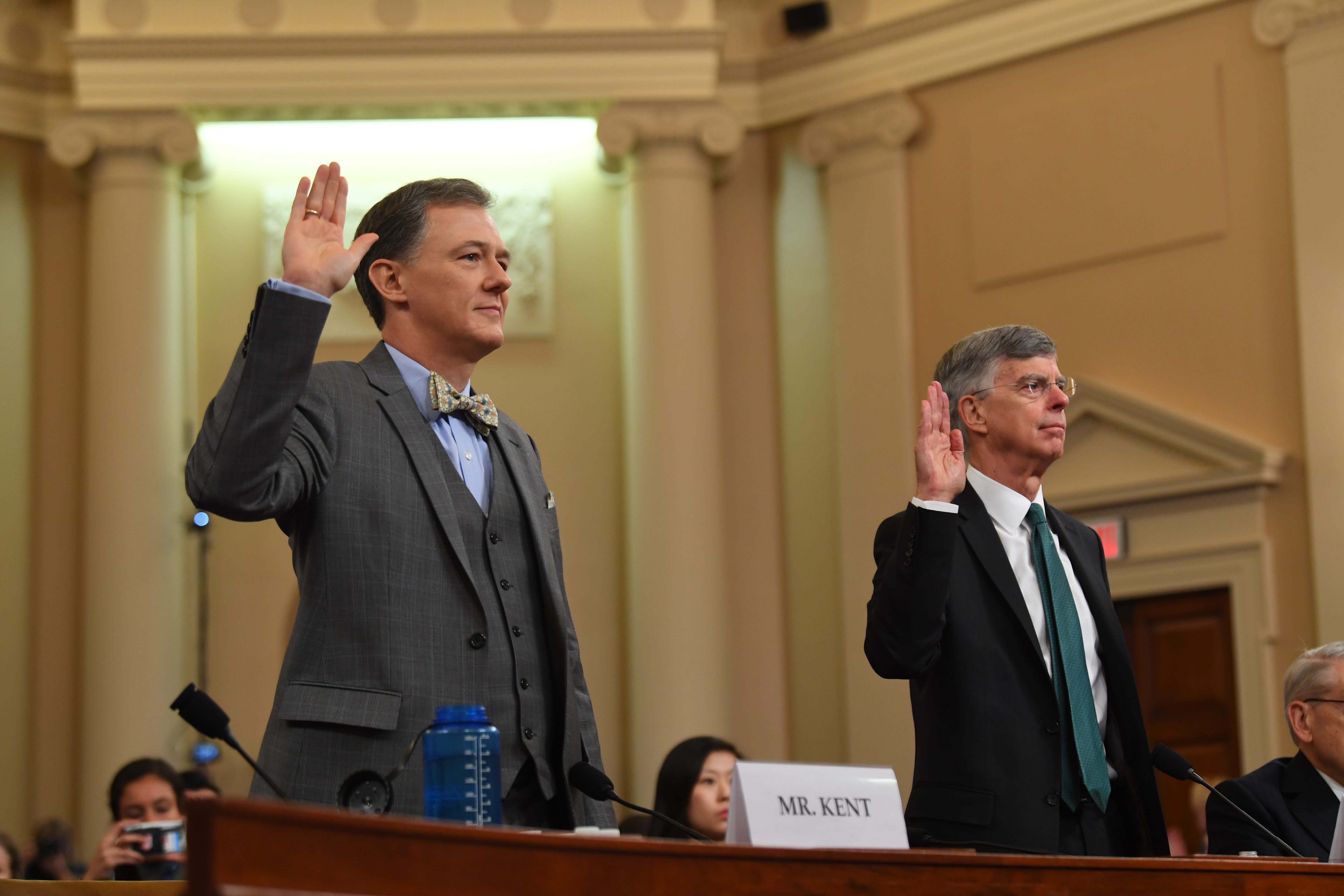 Kent and Taylor in the hearing room, raising their right hands to be sworn in.