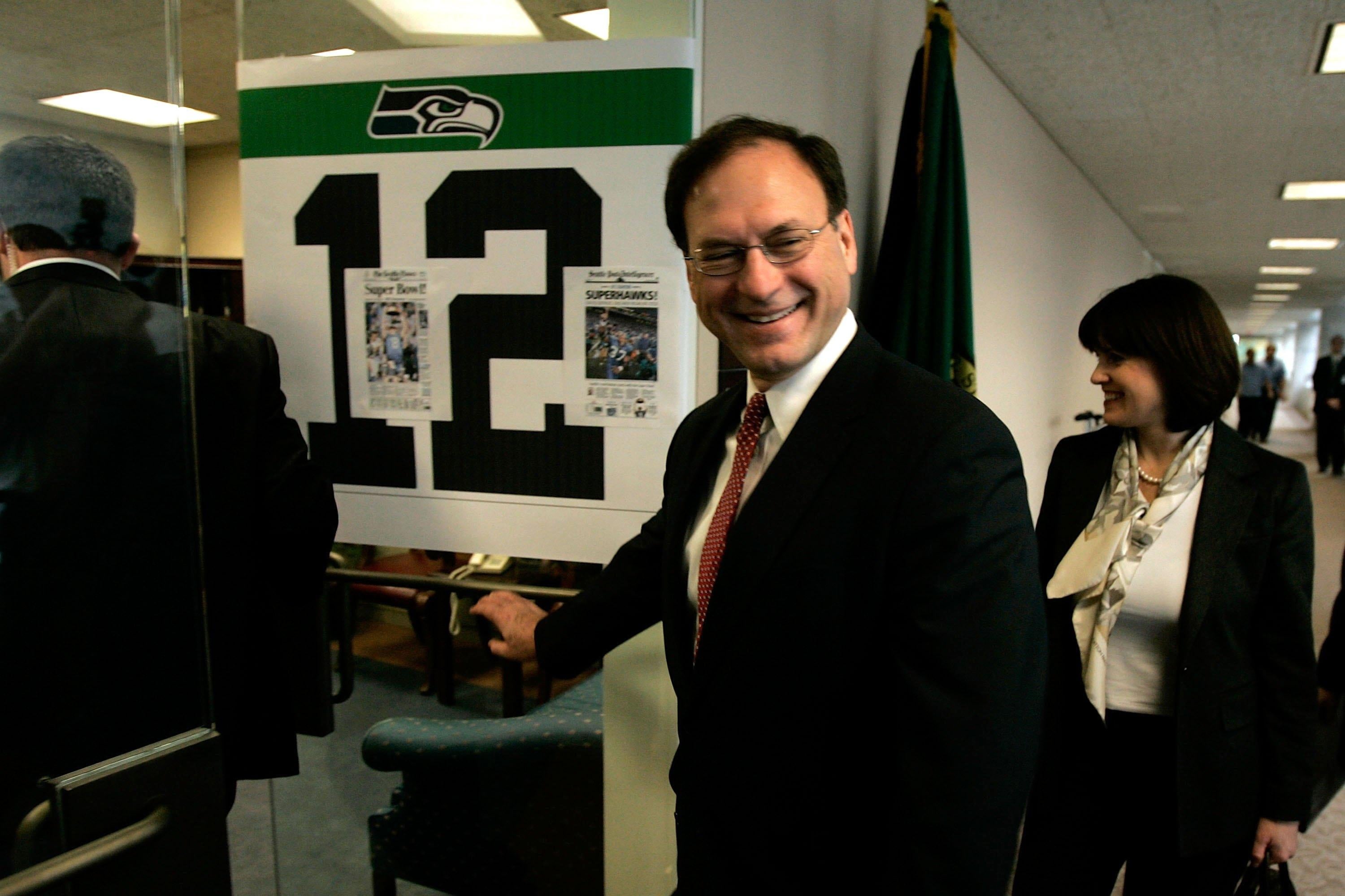 Alito visiting Maria Cantwell, grinning widely, and opening a door with a Seahawks logo on it.